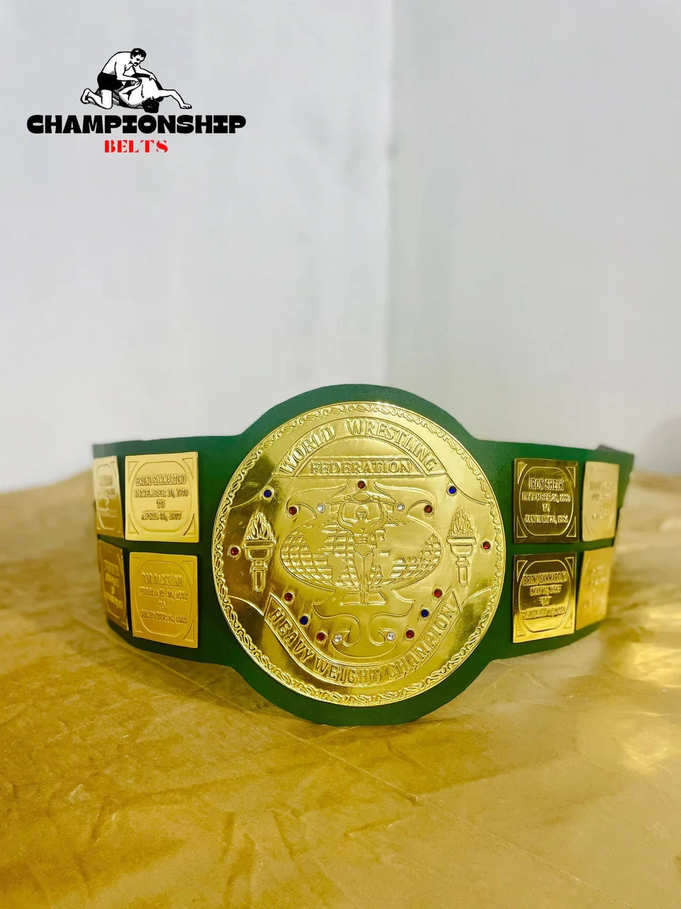 Gold championship belt with green strap on a white background, featuring the Championship Belts logo.